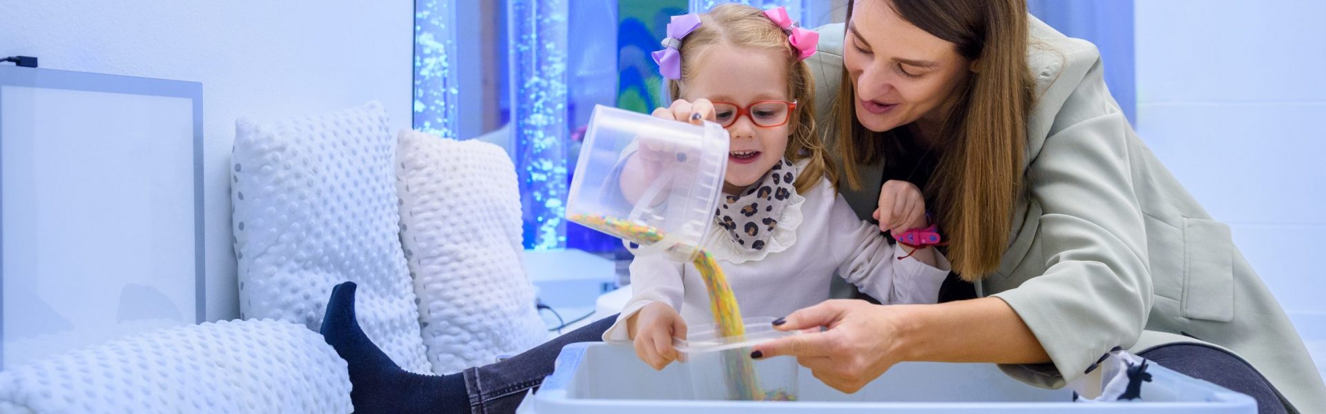 Child with physical disability in sensory stimulating room, snoezelen. Child living with cerebral palsy interacting with her therapist during therapy session.